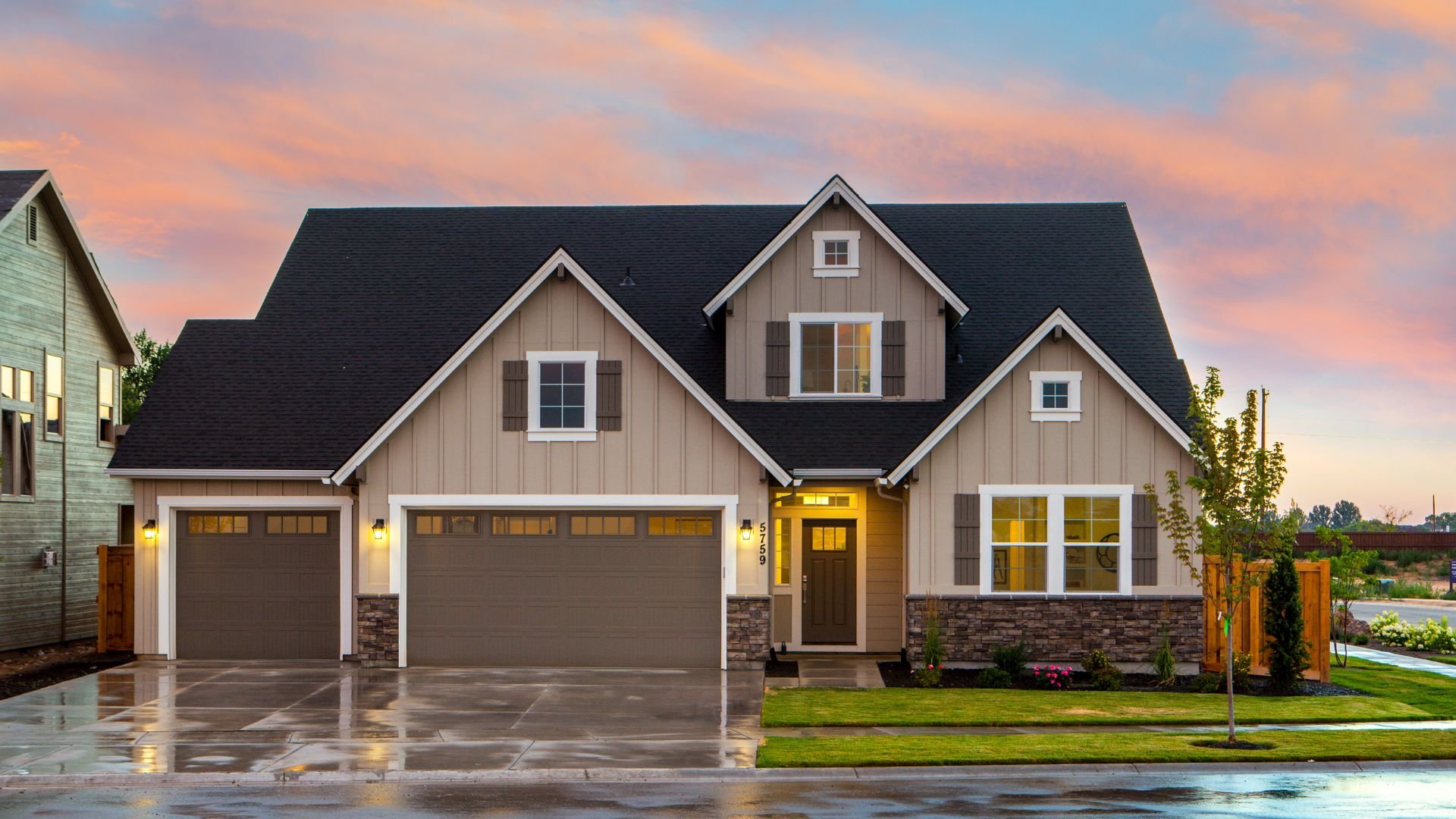 Modern two-story house with stone accents and wet driveway at sunset