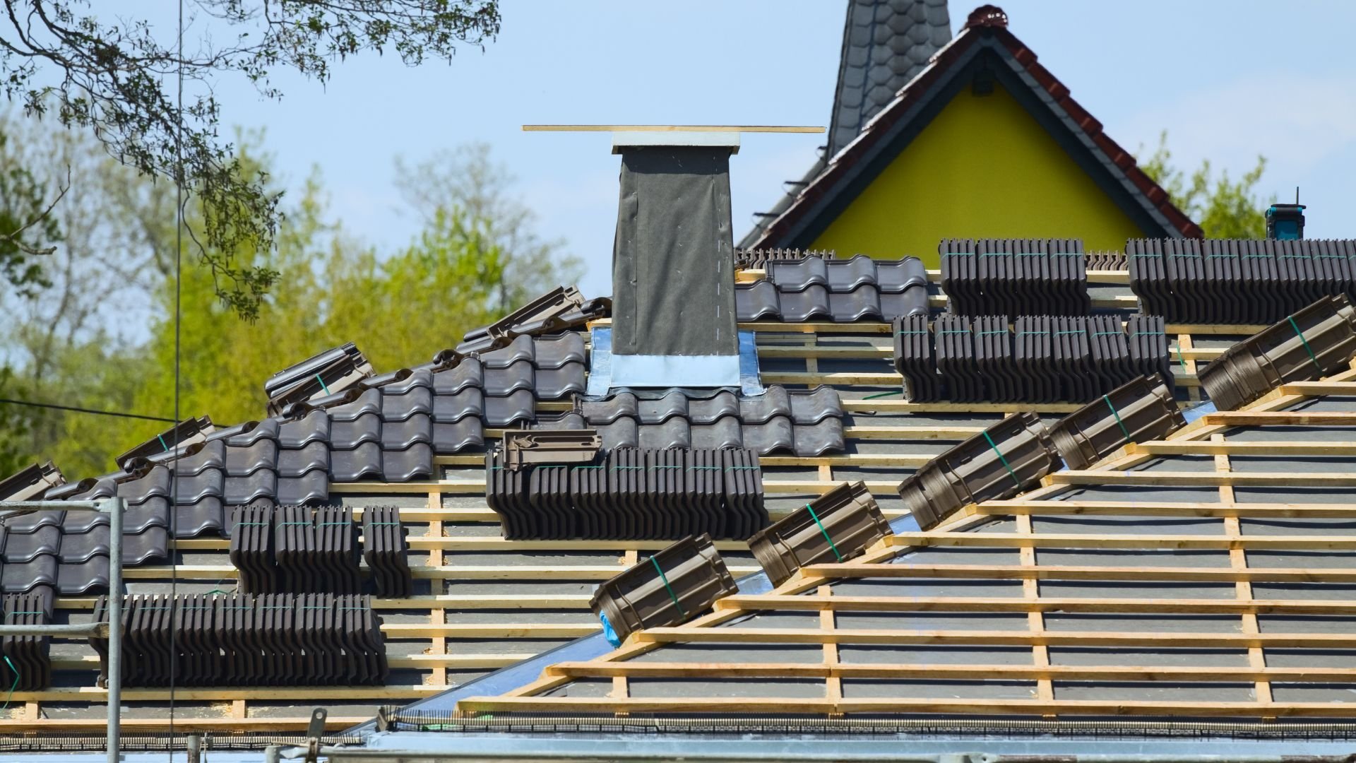 Roof under construction with tile stacks and wooden battens near yellow house