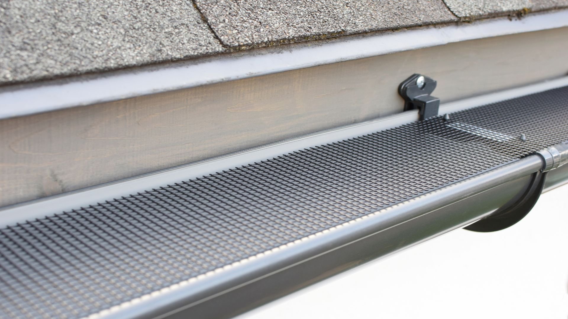 Gutter guard with metal mesh installed on roof edge under shingles