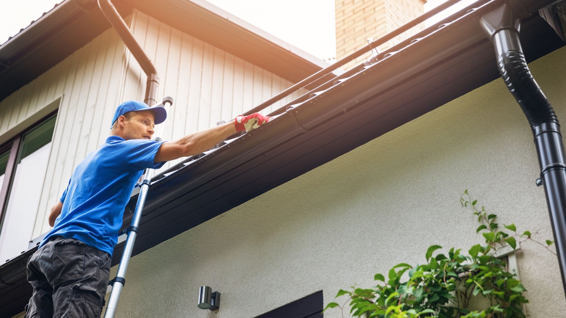Worker on ladder cleaning gutters of residential house exterior