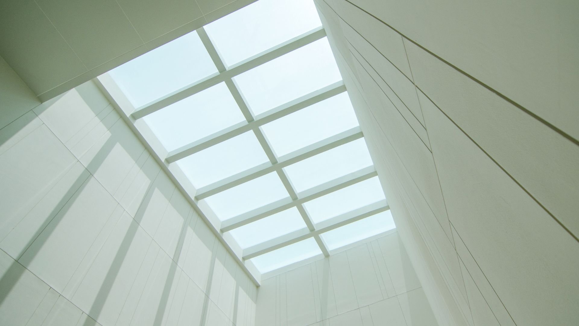 White geometric skylight illuminating modern, minimalist tiled interior space