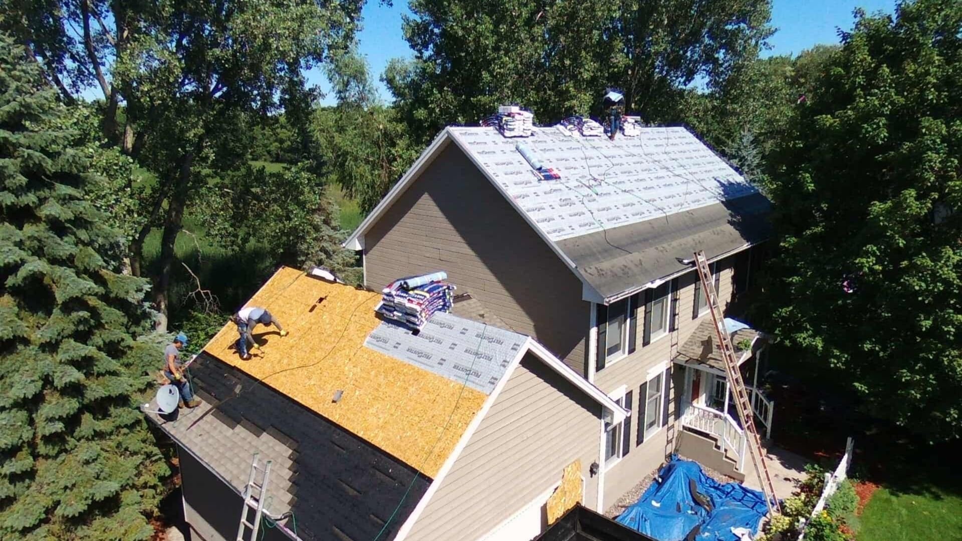 Roofers installing new shingles on a multilevel house surrounded by trees